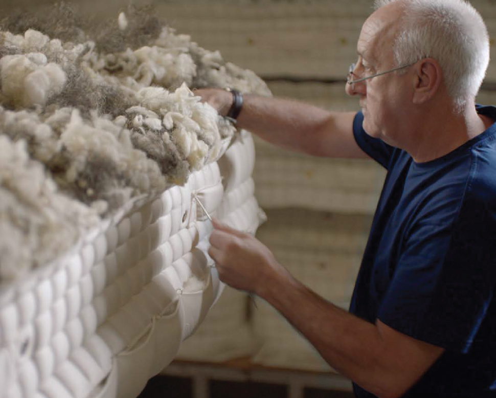 Factory worker hand stitching a mattress